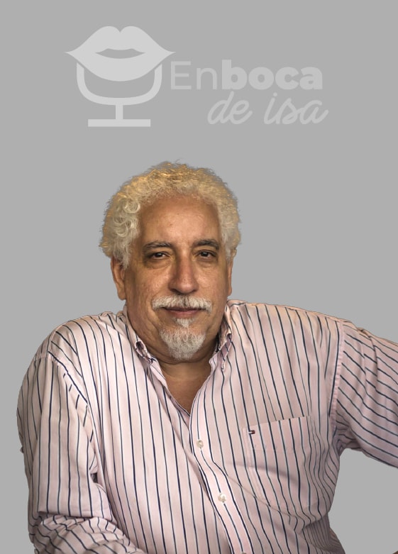 Un hombre de pelo blanco rizado y barba, que viste una camisa a rayas rosas y blancas, está sentado sobre un fondo gris con el logo "Enboca de Isa" sobre él. Esta escena es el escenario perfecto para la interesante charla de Isabel Restrepo sobre la mentoría en Miami.