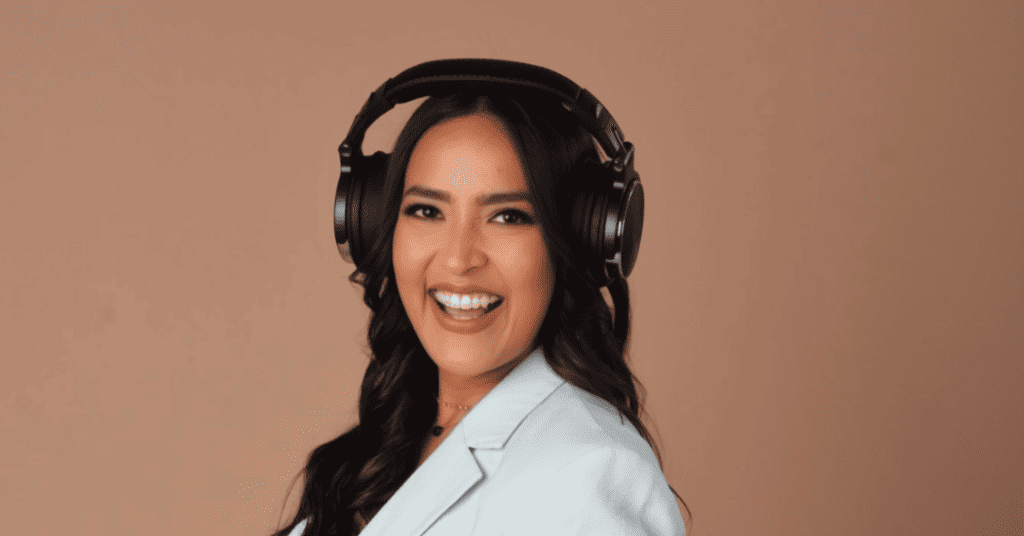 Isabel Restrepo, una mujer de cabello largo y oscuro, sonríe mientras usa grandes auriculares supraurales y un blazer de color claro sobre un fondo liso, capturando la esencia de Speaker Miami.