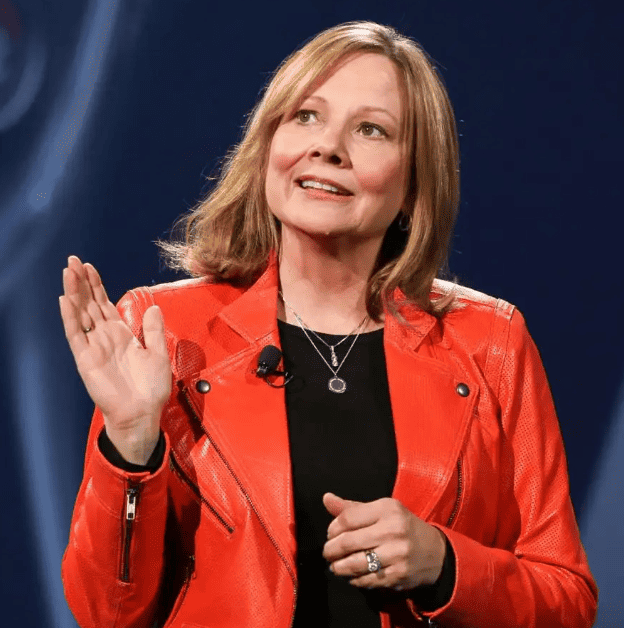 Una persona con cabello hasta los hombros y una chaqueta roja brillante, identificada como Isabel Restrepo, habla en el escenario con una mano levantada.