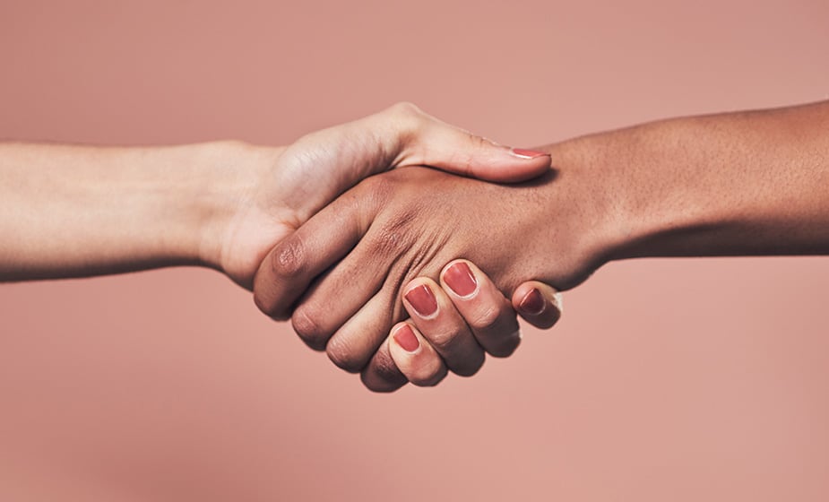 Dos manos, con diferentes tonos de piel, se estrechan las manos sobre un fondo rosa claro, simbolizando el espíritu de colaboración y conexión que define a Mentoring Miami.