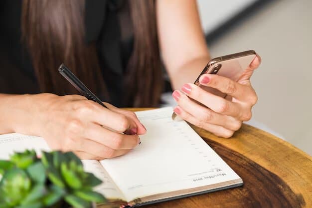 Una persona con cabello largo escribe en un cuaderno, anotando cuidadosamente los puntos de su agenda, mientras sostiene un teléfono inteligente en la otra mano.