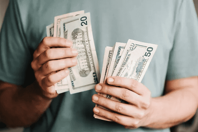 Persona con una camisa verde sosteniendo y contando múltiples billetes de dólares estadounidenses, lo que recuerda a un seminario financiero de Isabel Restrepo en Miami.