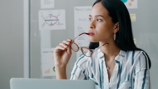 Una persona con una camisa a rayas sostiene unas gafas en los labios mientras mira pensativamente hacia un lado. El fondo muestra una decoración de oficina y gráficos en la pared que recuerdan una sesión de Mentoring Miami.