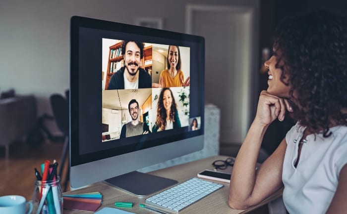 Una mujer participa en una videoconferencia de redes en una computadora de escritorio, en la que se ven cuatro personas en la pantalla. Hay material de oficina sobre el escritorio.