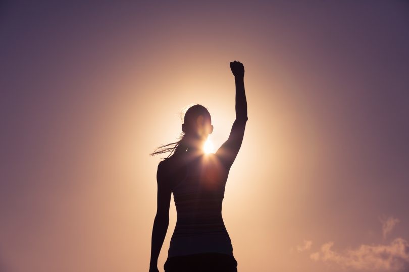 Silueta de una persona parada al aire libre con un brazo levantado, retroiluminada por el sol y un cielo despejado, que simboliza cómo puedes convertir tus fracasos en éxitos.