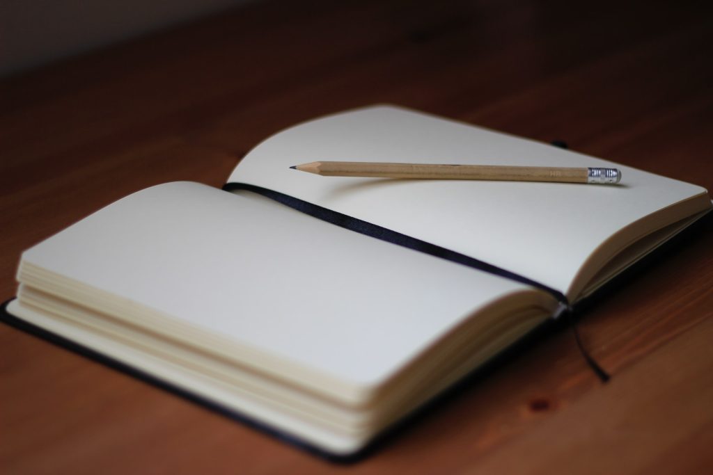 Un cuaderno en blanco abierto con un lápiz de madera apoyado entre sus páginas sobre una superficie de madera, que te invita a escribir sobre tus emociones y fomentar la autocomprensión.