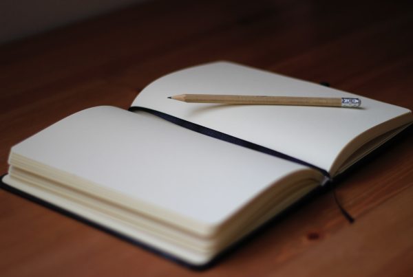 Un cuaderno en blanco abierto con un lápiz de madera apoyado entre sus páginas sobre una superficie de madera, que te invita a escribir sobre tus emociones y fomentar la autocomprensión.